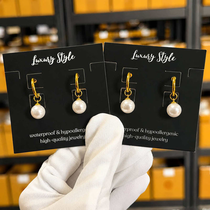 Gold Steel Stud Earrings in gold-tone metal with dangling white pearl-like beads on black display cards