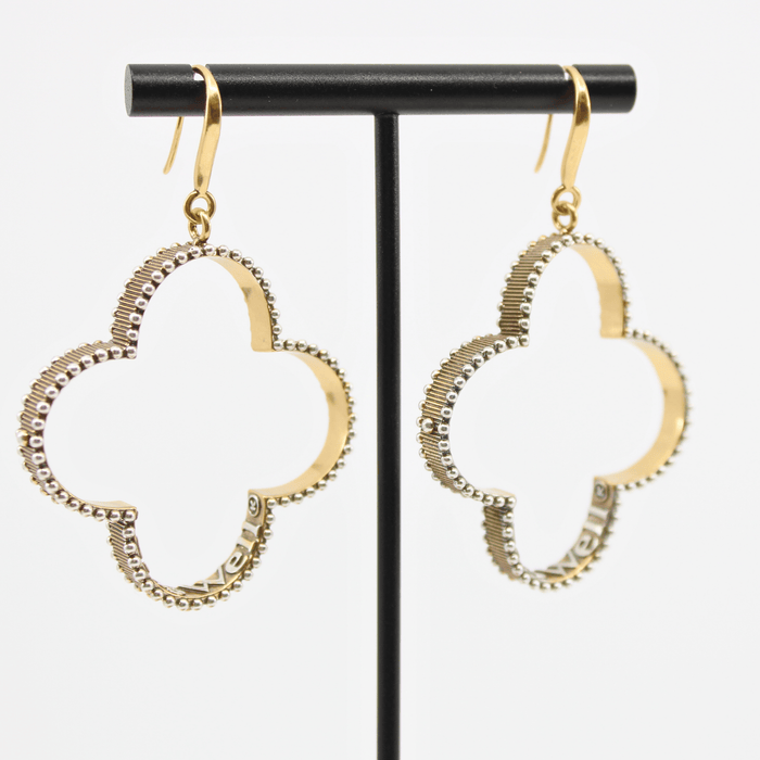 A pair of gold-colored composite drop earrings with French ear wire, featuring a clover design with a message inscribed inside, displayed on an earing stand.