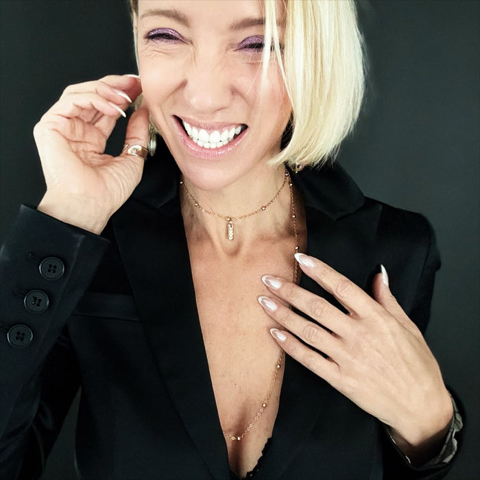 Woman wearing a black blazer with a necklace, against a dark background