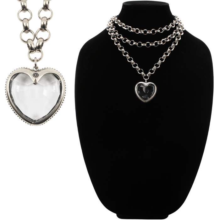 Silver chain necklace with heart-shaped pendant on a black stand, with another heart-shaped pendant on a chain on the left.