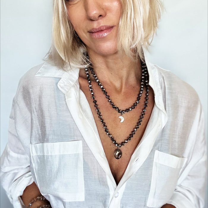 Woman wearing a white shirt and multiple necklaces against a plain background