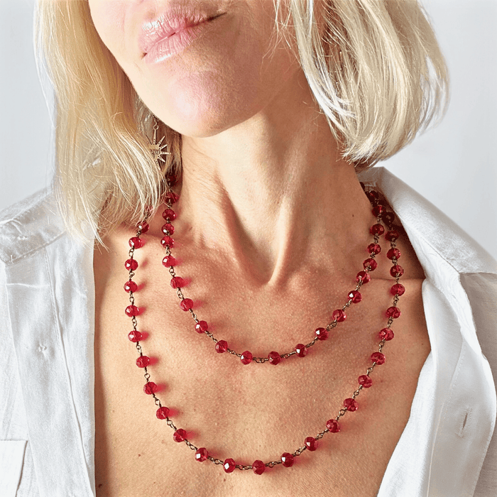 Close-up of a person wearing a red beaded necklace against a plain background