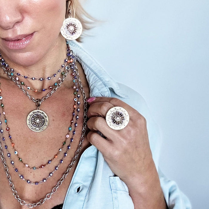 Woman wearing layered necklaces and earrings against a light blue background