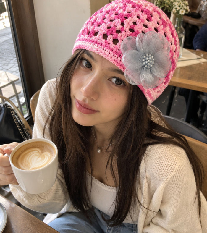 Pink crocheted beanie with patterned holes and large gray tulle flower on front