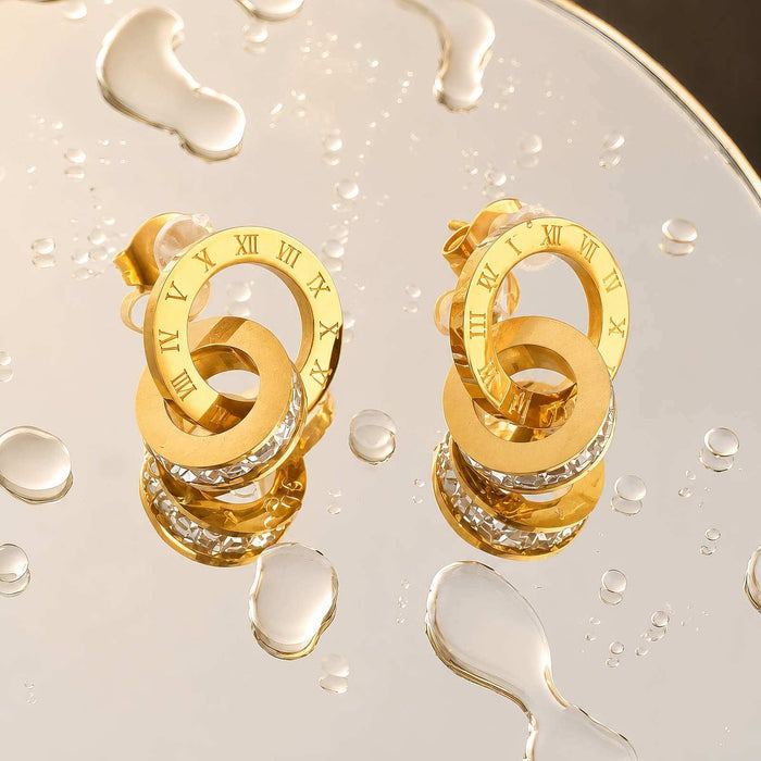 Gold Steel Stud Earrings in a polished gold-tone finish, featuring layered interlocking loops with Roman numeral details and clear stones