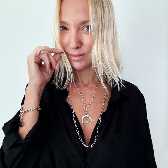 A person wearing a black shirt and showcasing a silver-colored necklace with a crescent moon pendant and a paperclip chain.
