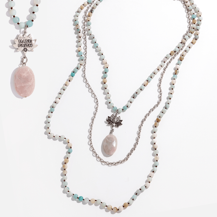Two views of a long beaded necklace with a lotus pendant and a faceted peach quartz drop stone, with one showing the front and the other showing the back with the inscription 'HAVE FAITH'.