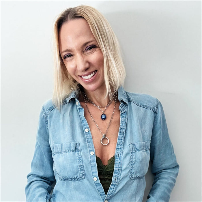 A person wearing a denim shirt and a necklace with a circular pendant.