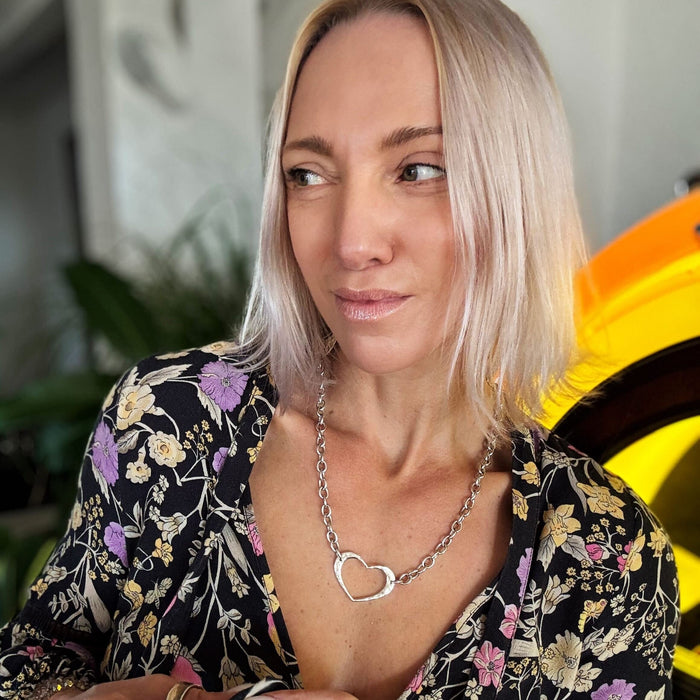 Woman wearing a floral top and heart-shaped necklace with a blurred background