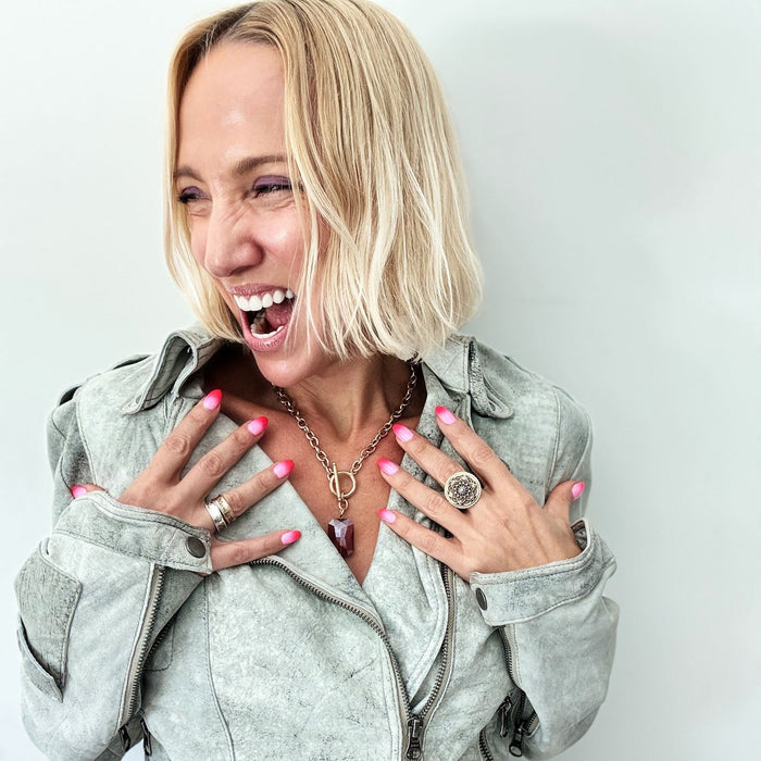 Woman wearing a light gray jacket with visible jewelry against a plain background