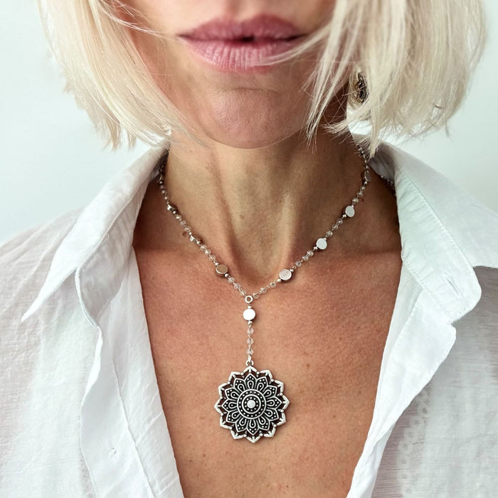 Woman wearing a silver necklace with a mandala pendant against a white background