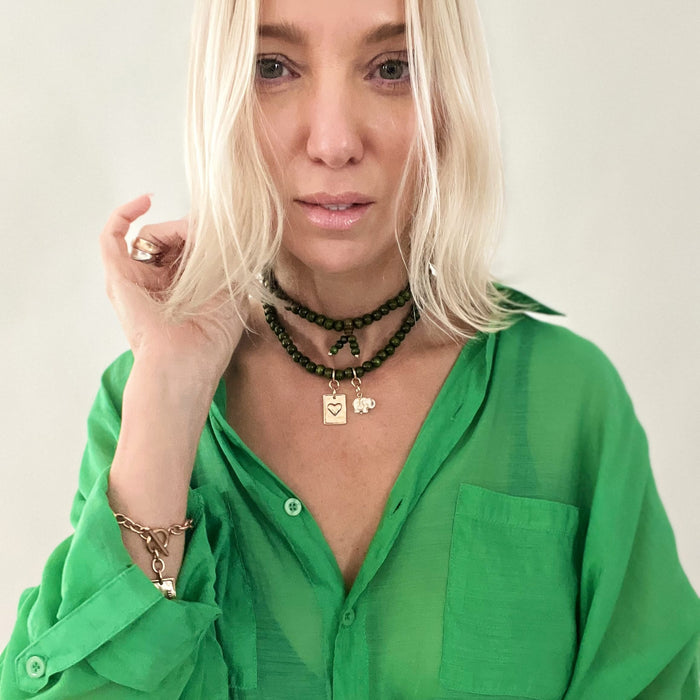 A person wearing a green shirt and showcasing a wooden boho wrap bracelet with a gold finish pendant and an off-white howlite elephant charm.